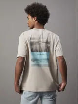 Remera color beige de algodón regenerativo con cuello redondo, mangas cortas y logo CK bordado en el pecho. Presenta un diseño de paisaje gráfico en el frente.