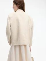 Blazer color crema con textura a rayas y lentejuelas. Tiene cuello con solapas, cierre frontal con botones, bolsillo en el pecho y apliques florales. Confeccionado en algodón y poliéster.