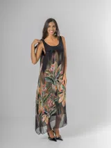 Vestido midi negro con estampado tropical de hojas y flores en tonos tierra, naranja y verde. Es de tirantes anchos con nudo regulable en el hombro y tiene aberturas laterales.