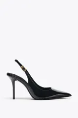 Zapato de tacón destalonado color negro charol, con punta fina y tira trasera con hebilla metálica dorada.