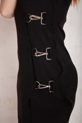 Vestido midi negro con escote en V, tirantes finos y abertura lateral. Presenta apliques metálicos en un lateral.