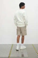 Short color beige de tejido grueso de algodón, con corte estándar, cintura elástica con cordón ajustable, bolsillos al bies y bolsillos de solapa con cierre autoadherente en las piernas y atrás.