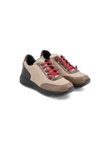 Zapatillas urbanas de cuero color beige con detalles en marrón y negro. Tiene cordones rojos, suela de goma negra y detalles en burdeos en el talón.