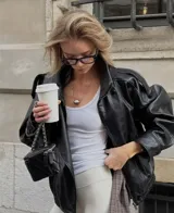 Chaqueta de efecto piel negra, con cuello alto estructurado y cierre asimétrico. Presenta un corte relajado y hombros ligeramente marcados.