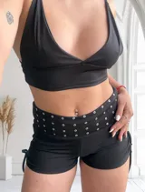Short negro ajustado con cintura ancha adornada con tachas plateadas y lazos laterales.
