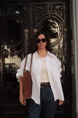 Bolso tipo tote de cuero color marrón con detalles de costuras trenzadas en los bordes y bolsillo externo. Tiene cierre imantado interno y broche con pasador de guampa en el exterior.