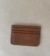 Tarjetero color marrón con textura símil reptil y costuras blancas. Tiene múltiples ranuras para tarjetas.