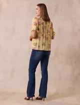 Blusa amarilla estampada con flores rosadas, de gasa, con cuello a la base, escote en V plisado y lazo de ajuste. Delantera con detalles en puntilla y mangas 3/4 con puño fruncido.