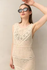 Vestido corto de crochet color crudo, sin mangas y con flecos en el ruedo.