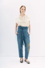 Pantalón de jean tiro alto con corte paper bag, lazo a tono en la cintura y bordado con lentejuelas y piedras en el lateral.