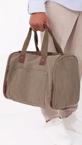 Bolso de lona color verde oliva con detalles en cuero marrón. Tiene apertura superior con cierre, bolsillos tipo guantera al frente, bolsillos interiores y amplios bolsillos laterales con cierre. Incluye doble correa de mano con agarradera forrada y correa larga desmontable y regulable.