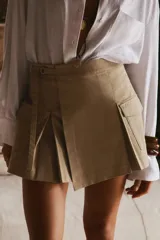 Falda pantalón color beige, de tiro alto, con bolsillos laterales tipo cargo, detalle de tablas y cierre lateral con cremallera oculta y trabilla con hebilla metálica.