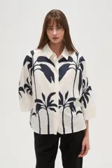 Camisa blanca con estampado de palmeras en color azul marino, de corte holgado, con cuello camisero, cierre frontal con botones y mangas 3/4 con puños anchos.