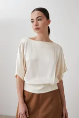 Blusa color beige, de tela satinada, con mangas cortas y cuello redondo.
