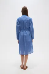 Vestido camisero de algodón color azul, de corte ancho y manga larga, con cuello camisero y lazo ajustable a la cintura.