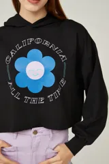 Buzo negro cropped con capucha y mangas largas abullonadas. Estampado frontal con una flor azul y texto en blanco.