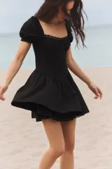 Vestido corto negro de popelín con escote cuadrado, mangas cortas abullonadas, bolsillos laterales ocultos y detalle de encaje a tono.