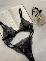 Conjunto de lencería de encaje negro con blanco, compuesto por un corpiño triangular con breteles regulables y cierre de gancho delantero, y una tanga regulable.