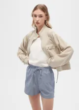 Campera color beige de manga larga, con cuello alto, cierre frontal con cremallera y botones a presión, bolsillos con solapa en el pecho y puños con trabilla ajustable.
