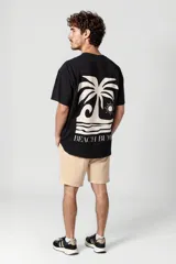 Remera negra con estampado de una palmera, el sol y olas, con la frase "Beach Bum" en blanco.