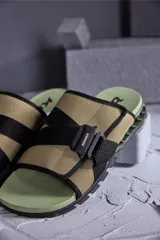 Sandalias tipo slide color beige con detalles en negro y suela verde.