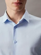 Camisa celeste de popelín de algodón elástico, corte slim, manga larga y cierre frontal con botones.