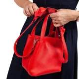 Cartera roja de cuero graneado con doble asa de mano y correa larga desmontable. Tiene cierre a presión y detalle de volado confeccionado a mano en cuero.