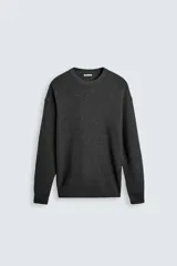 Sweater gris oscuro de punto perlado con cuello redondo y mangas largas. Tejido en hilatura de algodón y acabado en rib.