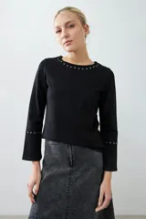 Remera negra de manga larga con cuello redondo y tachas plateadas en el cuello y los puños.