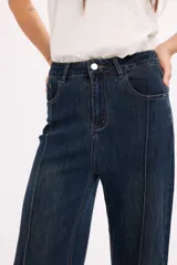 Pantalón de jean azul oscuro de tiro alto, con costuras verticales decorativas en el frente y cierre de botón metálico.