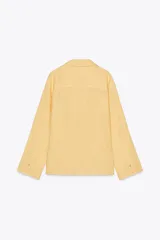 Camisa de lino color amarillo claro, de corte recto, con cuello solapa, escote en pico, cierre frontal con botones y mangas largas con puños abotonados.