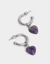 Aros dorados tipo argolla con dije colgante de cristal transparente en forma de corazón.