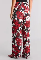 Pantalón pijamero de satén calado estampado con flores rojas y blancas sobre fondo negro, de calce relajado, cintura elastizada y bolsillos ocultos.