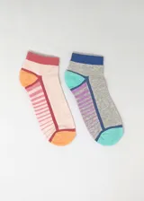 Pack de dos pares de medias tobilleras con diseños coloridos. Un par es color crema con rayas horizontales rosas, talón y puntera naranja, y borde superior rosa. El otro par es gris con rayas horizontales violetas, talón y puntera celeste, y borde superior azul.