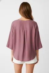 Blusa blanca de algodón con broderie, corte holgado, cuello en V y mangas 3/4 con botón para sujetar.