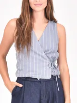 Chaleco sin mangas de color beige con rayas verticales blancas. Presenta un diseño cruzado tipo wrap con escote en V y ajuste mediante lazo lateral.