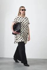 Vestido corto de silueta amplia con corte bajo busto, cuello a la base y mangas cortas. El tejido presenta un estampado de hojas en tonos rojo óxido y turquesa sobre un fondo de rayas verticales blancas y negras.