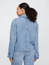 Campera de jean celeste, corte recto, con cuello clásico, cierre frontal con botones, mangas largas con puños abotonados, bolsillos de parche con solapa en el pecho y bolsillos laterales.