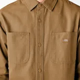 Camisa de manga larga color marrón con dos bolsillos frontales con botón y logo de la marca en uno de ellos.