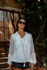 Camisa blanca de plumetí con cuello mao, mangas largas abullonadas con puños elásticos y cordón con borlas en el escote.