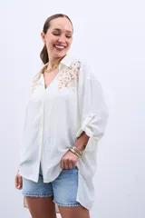 Camisa color crudo con bordado de lentejuelas doradas en el frente, de corte holgado y mangas largas con lazo en los puños.