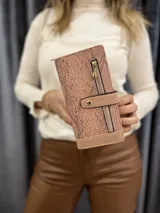 Billetera de cuero sintético color salmón con textura símil piel de serpiente. Tiene cierre dorado en el frente y correa con botón a presión.