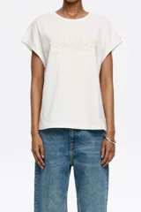 Camiseta blanca de algodón con corte recto, cuello redondo y mangas cortas tipo murciélago. Estampado frontal con el logo de la marca Bimba y Lola en color beige.