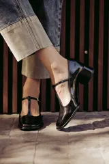 Zapatos de charol negro con diseño tipo T-bar, taco bajo cuadrado y punta redondeada.