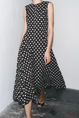 Vestido midi negro con estampado de lunares blancos, cuello redondo y sin mangas.