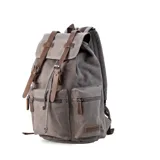 Mochila de tela canvas color verde oliva con tapa y detalles en símil cuero marrón. Cierre superior marinero, bolsillos internos, externos frontal, laterales y trasero con cierre. Asas rígidas, correas ajustables y espacio para laptop de 15".