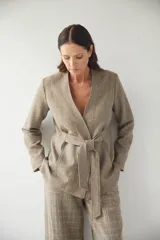 Chaqueta corta color beige, entallada, con escote en V, manga larga y cierre frontal con lazo fijo. Confeccionada en lana fina sin teñir, con bolsillos escondidos y terminaciones enviadas. Hecha 100% en Uruguay.