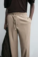 Pantalón color topo de corte recto, con cintura elástica ajustable con cordón, bolsillos laterales y bolsillos de vivo en la espalda.