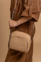 Bandolera de cuero sintético color beige, con diseño compacto y elegante. Cuenta con un bolsillo frontal con cierre y un compartimento principal con cierre. La correa es regulable.