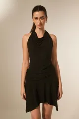 Vestido negro corto, ajustado al cuerpo, con cuello buche (drapeado) y frunces en la cintura. La falda tiene un ruedo asimétrico con volados.